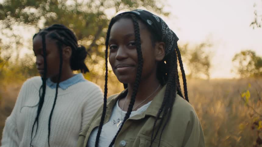 Two black teenagers stand in the woods near a sunset