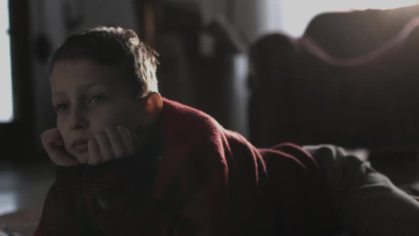 A sad looking boy lies on the floor at home and nervously looks up