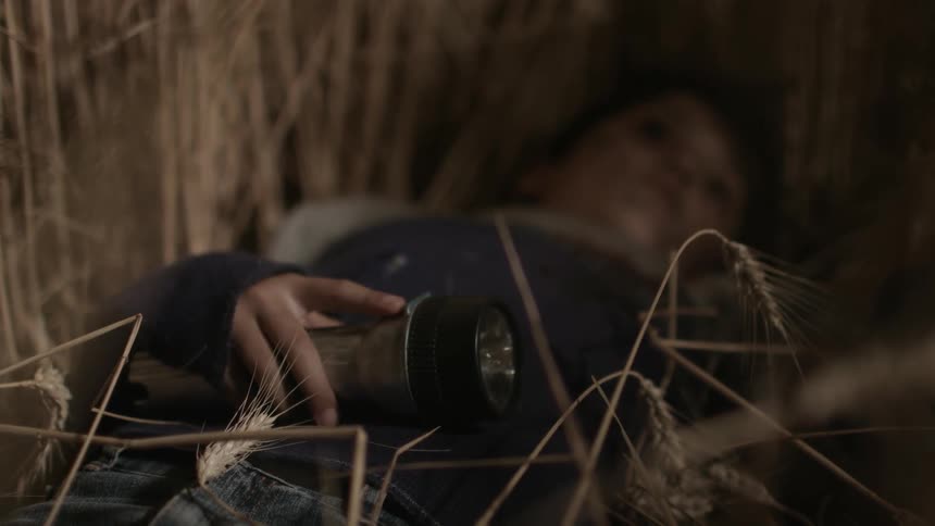 Boy holds flashlight in hand as he lays motionless on ground staring