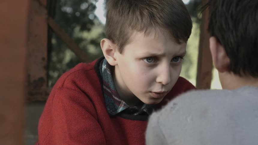 A boy stares intently at his friend while they sit on steps outdoors