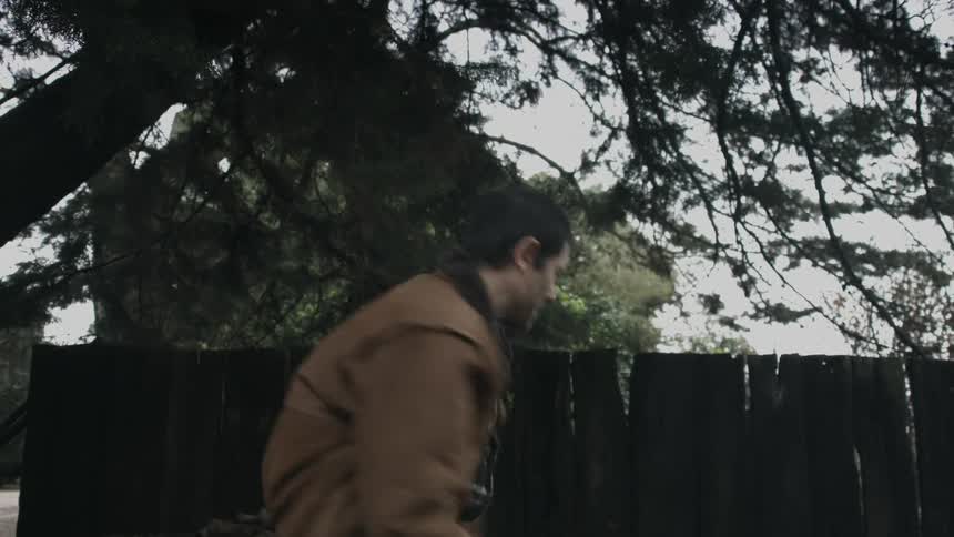 A man is standing outside as he raises his ax over his head and chops wood