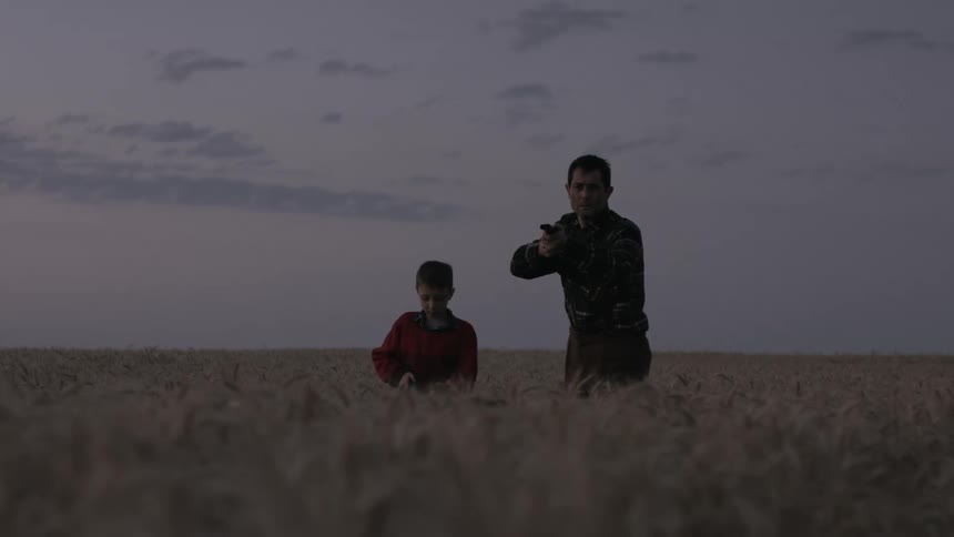 Son stands next to father aiming the rifle in the field at dusk