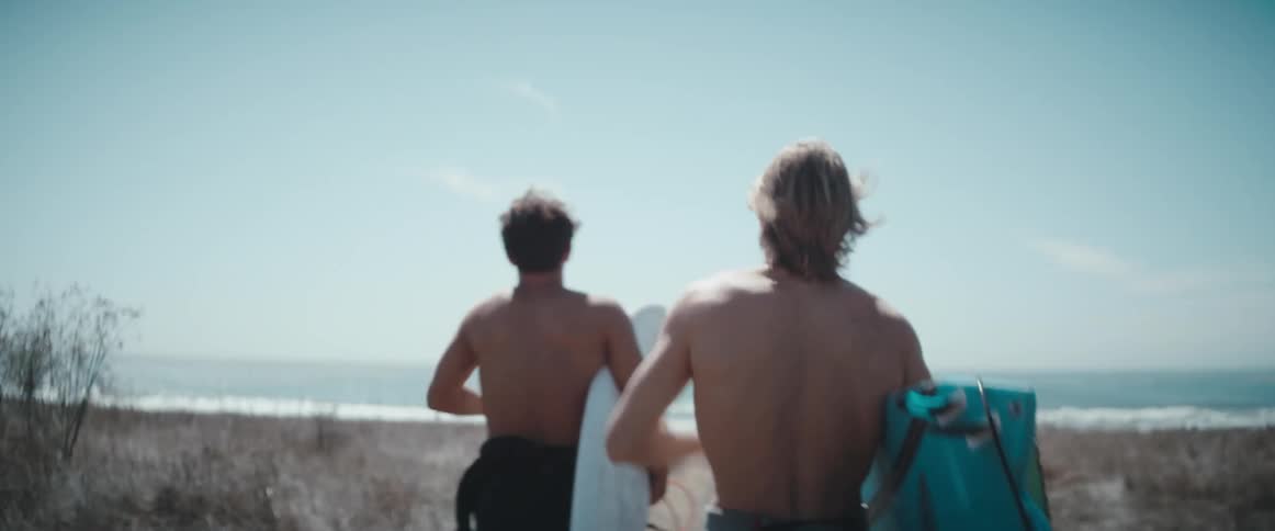 Two men run toward the beach with their surfboards