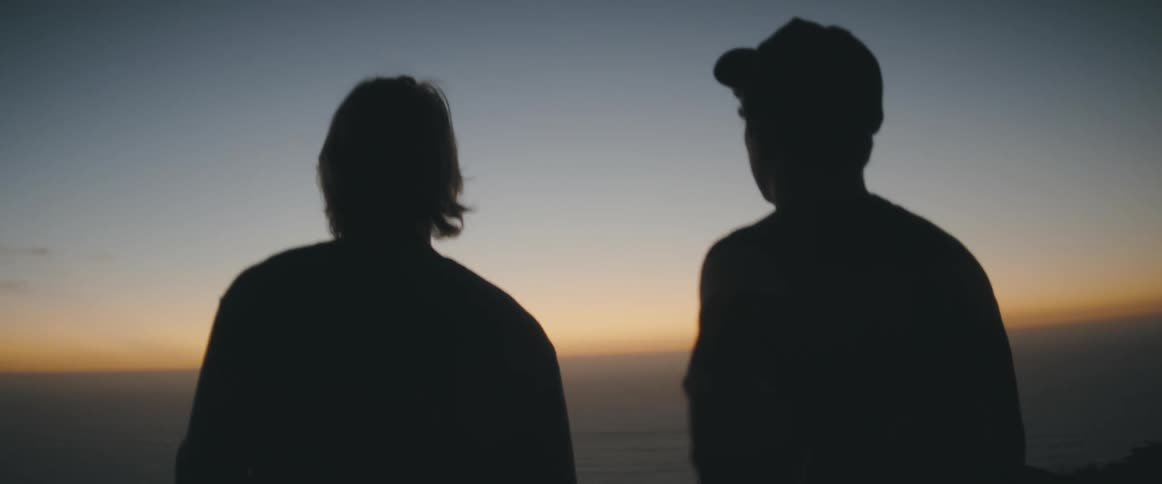 Two men walk toward a sunset to take a photo