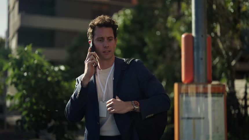 Man talking on smartphone checks watch then ends call and walks past bus stop