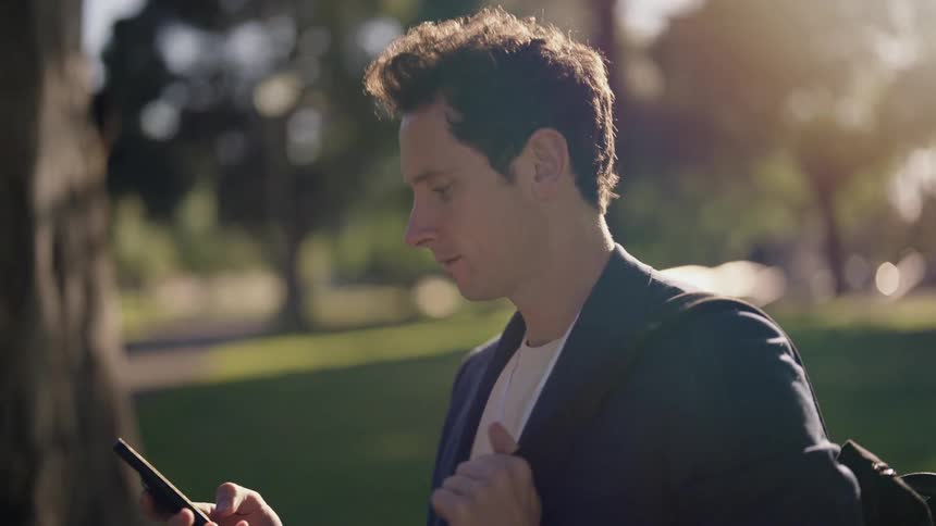 A young man walks past a public park as he looks at his cell phone
