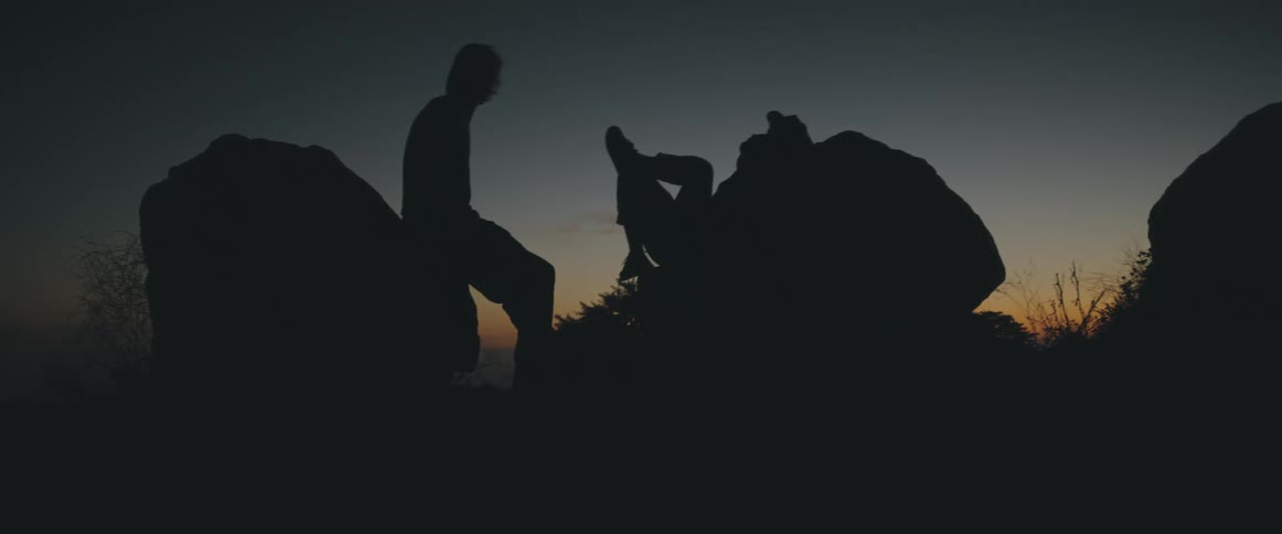 Two people lean on rocks in the sunset