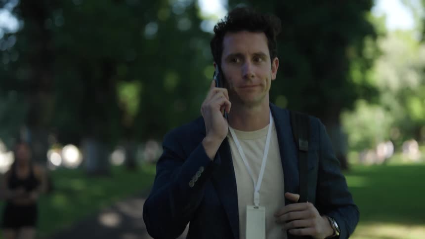 Young man talks on his smartphone while walking through a park in the city