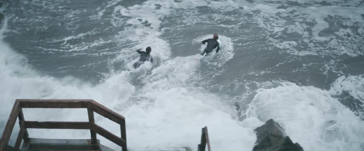 Two surfers jump into the water with their boards