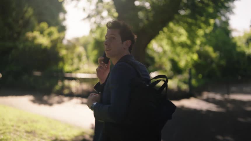 A man talks on the phone while walking along a park trail