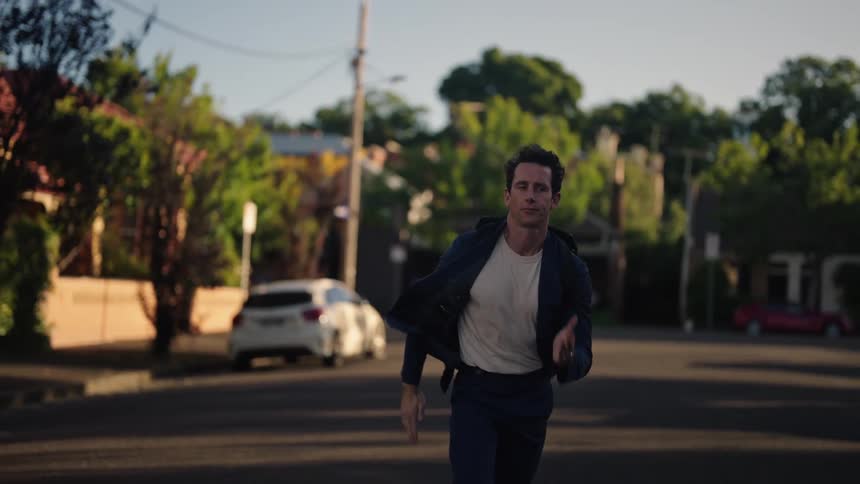 Man with backpack blazer jacket white shirt and pants runs on the street checking watch in the neighborhood