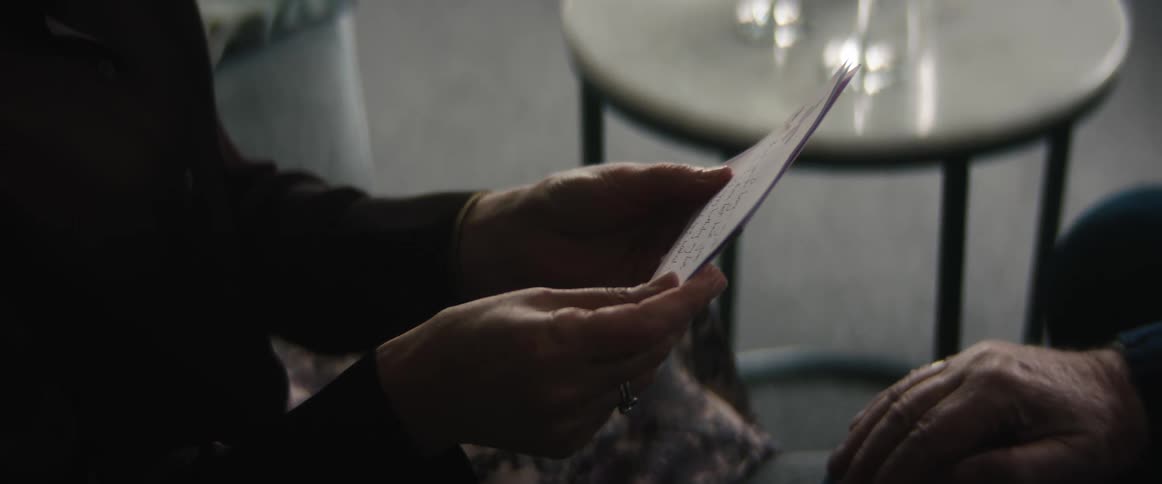 Woman reads note while sitting facing elderly man then reach out to touch him