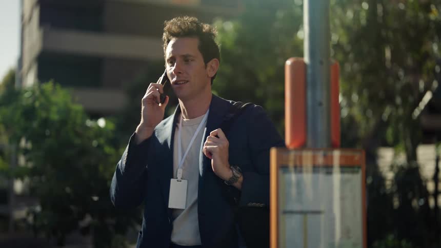 Young man standing impatiently on a bus stop in the city talks on his smartphone