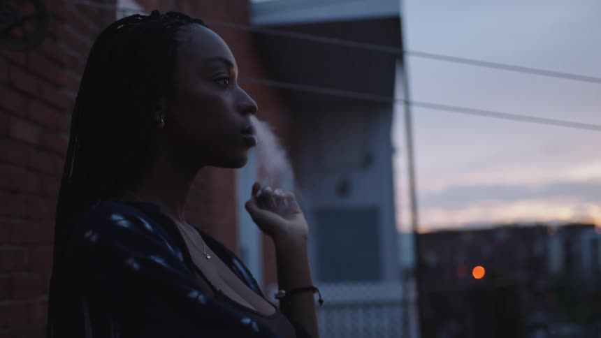 A woman smokes a cigarette outside her apartment building