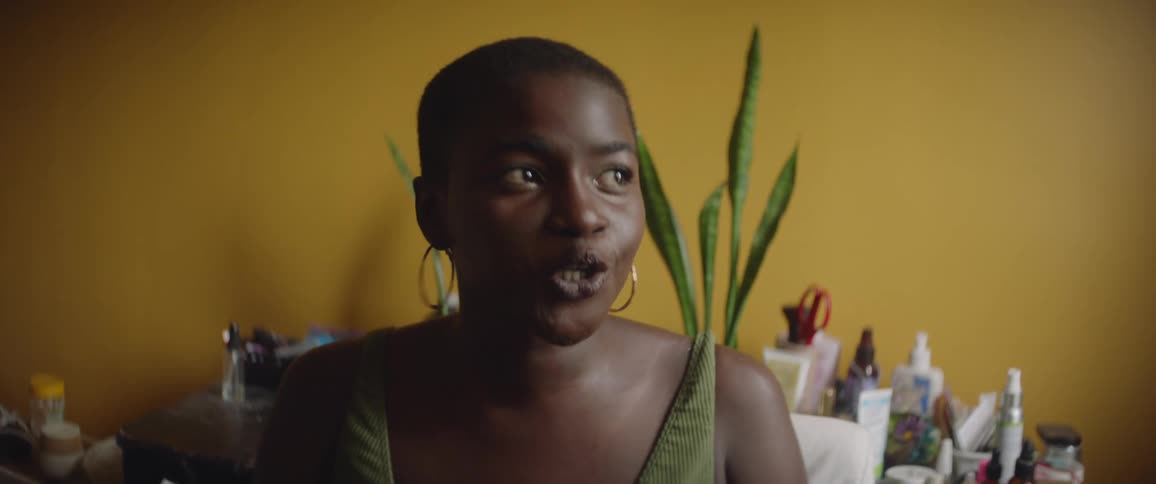 A woman is sitting down in a room smiling as she speaks to someone
