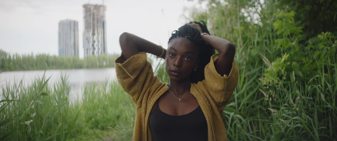 A black girl plays with her hair standing by a lake