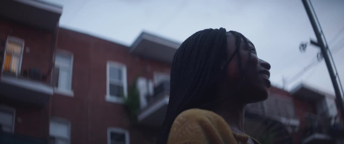 A woman is standing outside of an apartent building speaking to someone