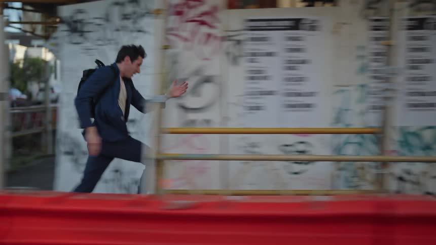 A young man runs down a city street as he looks at his watch