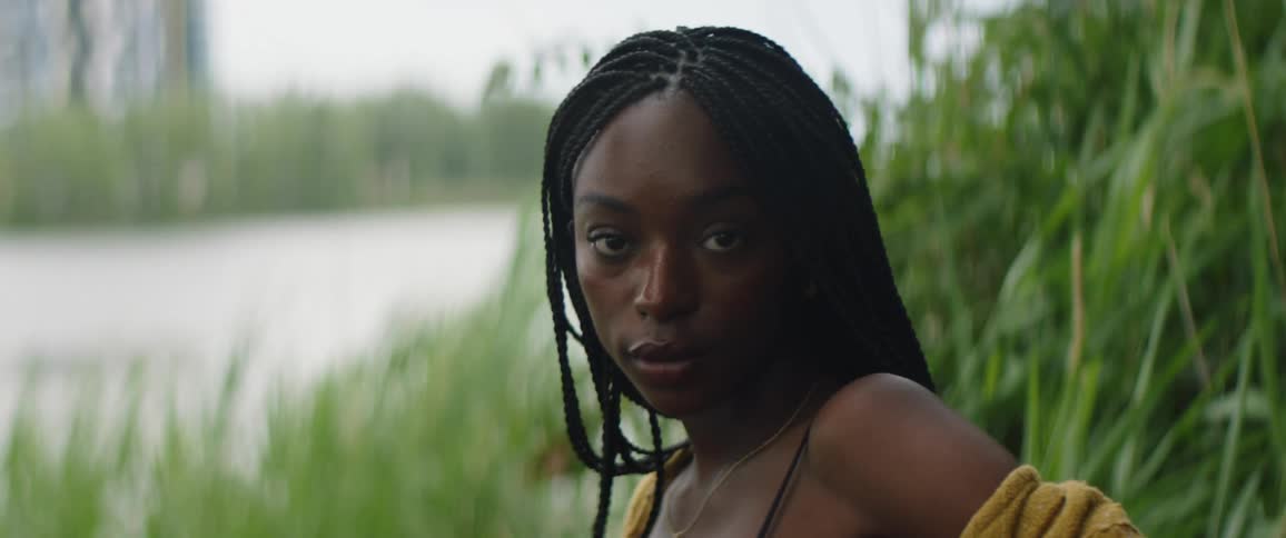 Female model with braids and yellow jacket looks at camera near the river