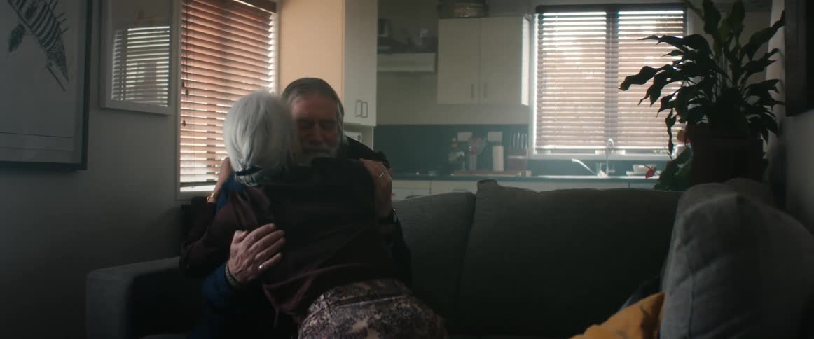Elderly couple sitting in the couch at home talk and hug