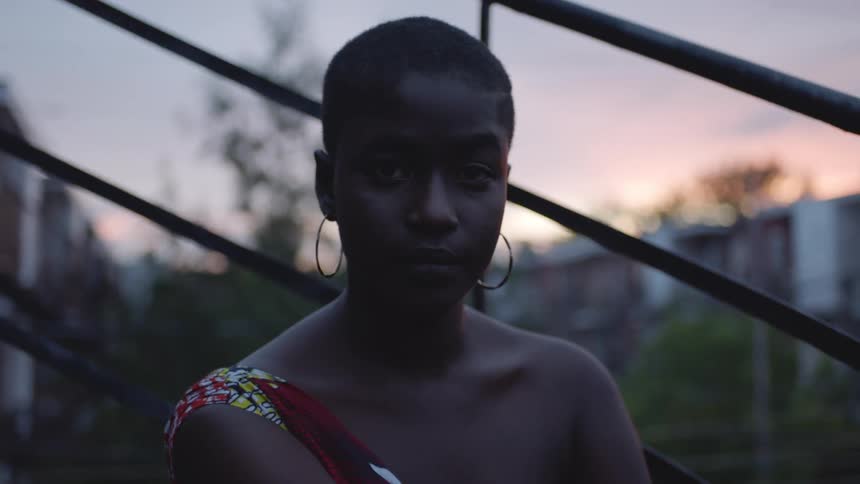 Woman with hoop earrings and revealing blouse stares at the camera at dusk