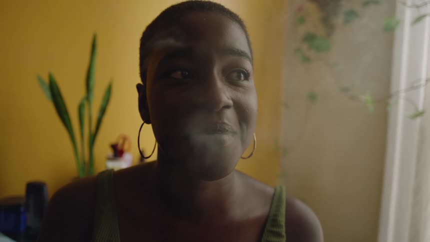 A young woman is smoking a cigarette inside of there home in the day time
