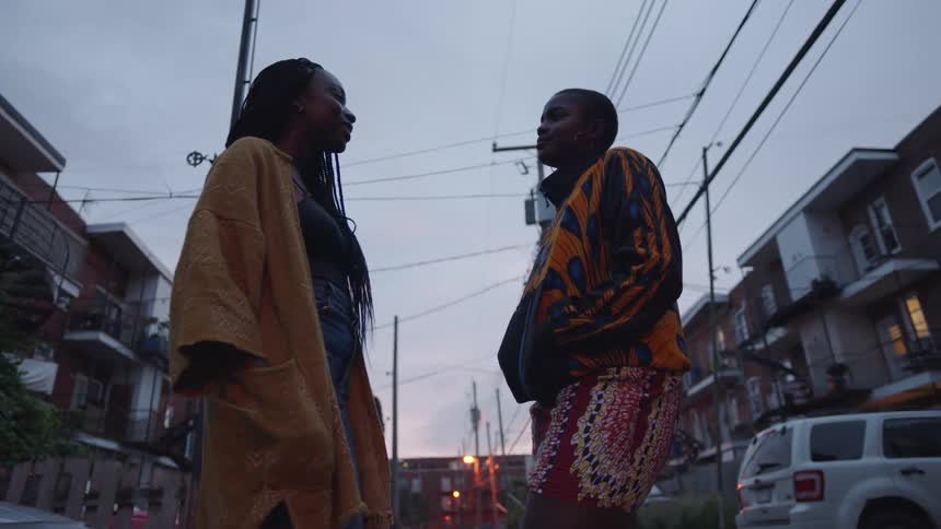 Two friends wearing colorful outfits talk on the street of a neighborhood