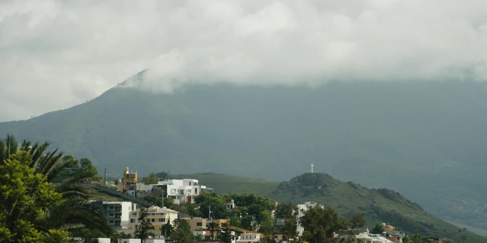 Buildings on hill slope and high mountains with clouds in the background