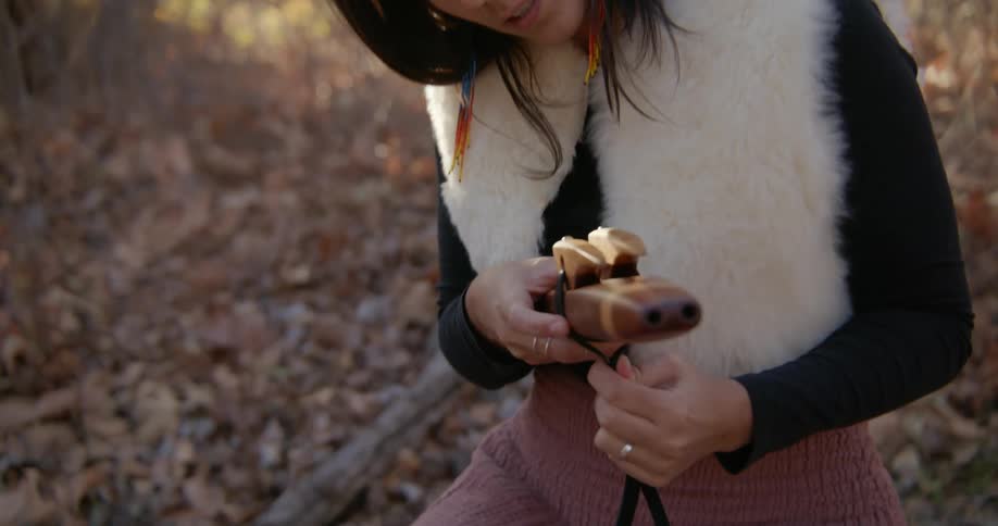 Young woman sitting outdoors wearing a fur coat wrapping a wooden tool at evening