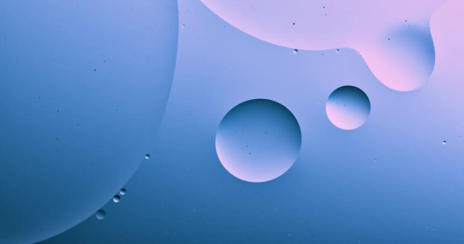Blue and pink pastel light shines on a substance as droplets move inside the liquid and they merge and become one when they touch