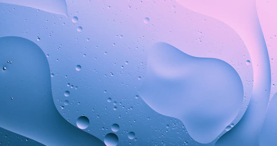 Blue and pink pastel light shines on a substance as droplets move inside the liquid