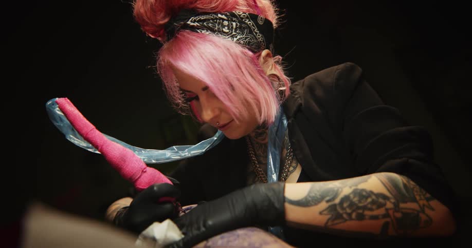 Close up of a tattoo artist with colorful hair working on the skin of a client