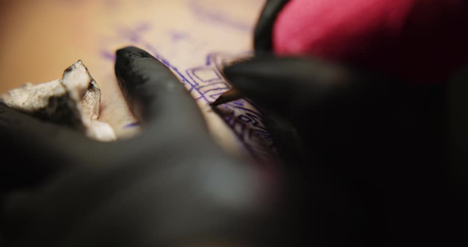 A persons back is shown getting a tattoo from a tattoo artist whose hands are the only body part shown