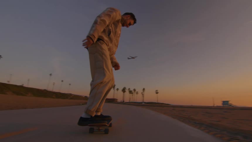A man jumping on a skateboard while riding on a beachfront sidewalk at sunset