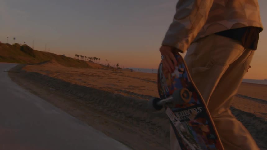 A man riding a skateboard on a beach sidewalk at sunset
