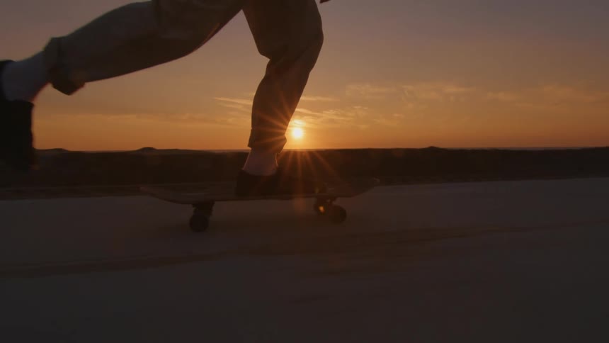 A man is riding a skateboard on a road along the coast with the sun setting in the distance