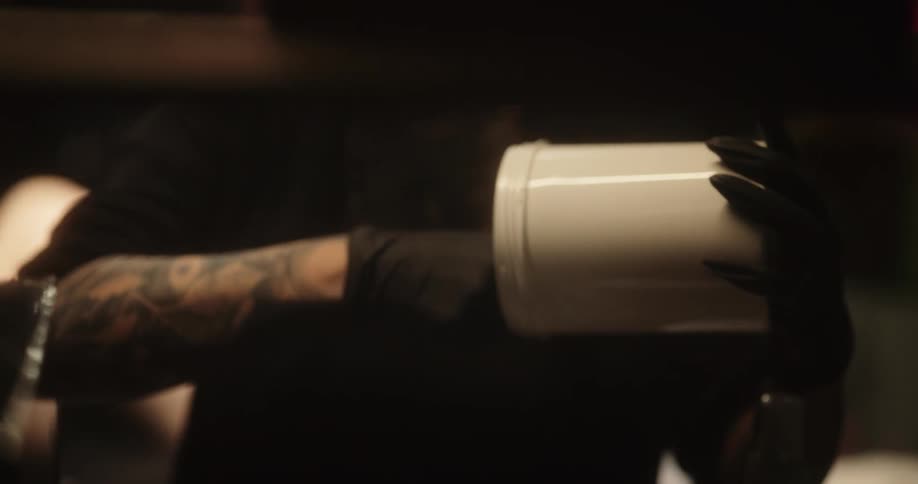 Tattoo artist mixes a gel inside a plastic container with a wooden tool