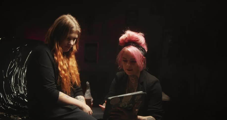 A tattoo artist shows a woman a tablet as she points to the customers thigh