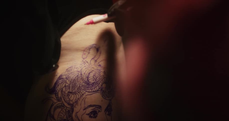 Tattoo artist uses a drawing as reference to sketch a tattoo on the skin of a client