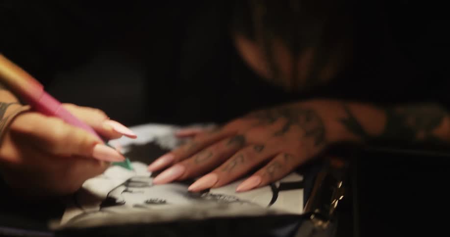 Close up of a tattoo artist sketching on a piece of paper with a pen
