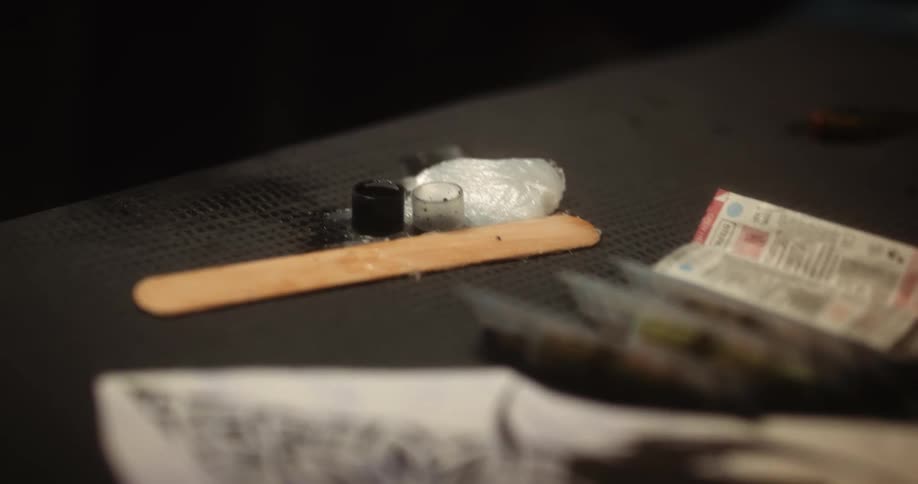 A tattoo artist dips her needle in a tiny ink container sitting on a table
