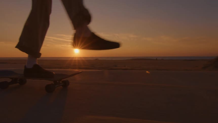 A skateboarder skates down a road along a beach at sunset