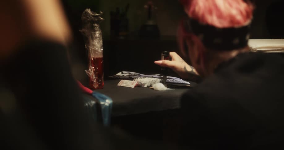 Close up of a tattoo artist with colorful hair mixing inks over a table