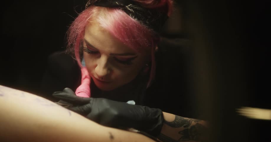 Close up of a tattoo artist with colorful hair working on the skin of a client