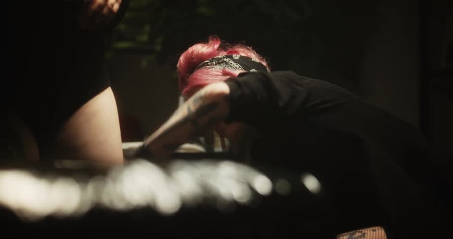 A tattoo artist with pink hair wiping a clients leg