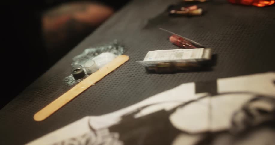 An employee at a tattoo parlor dips equipment in ink while looking at a portrait