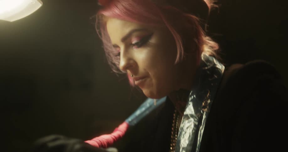 Close up of a tattoo artist with colorful hair working on the skin of a client