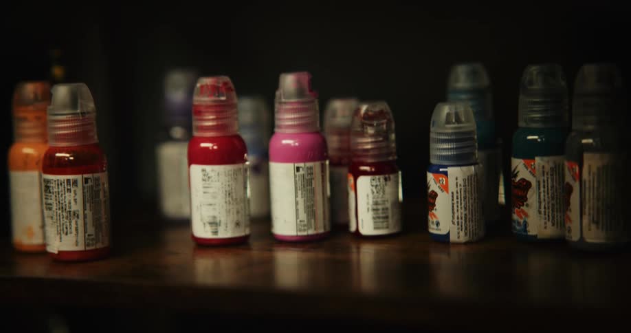Several bottles of different color paint are on a wooden shelf