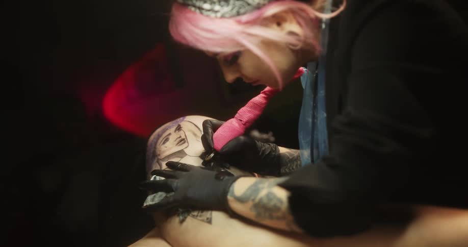 Close up of a tattoo artist with colorful hair working on the skin of a client