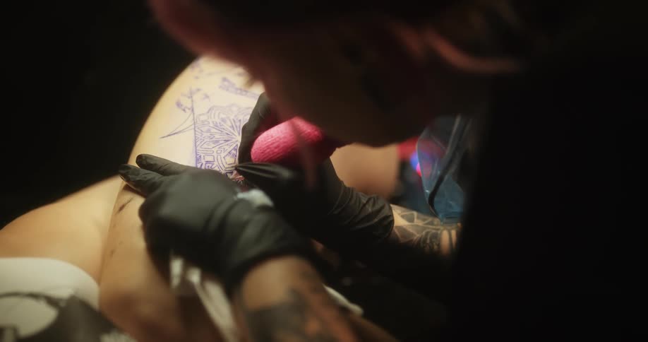 A woman tattoos another womans thigh who is laying down